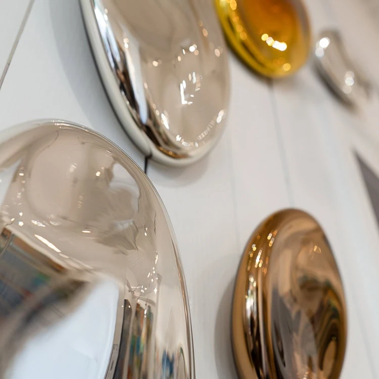 Close-up of reflective, smooth, oval-shaped metallic objects mounted on a light-colored wooden wall panel.